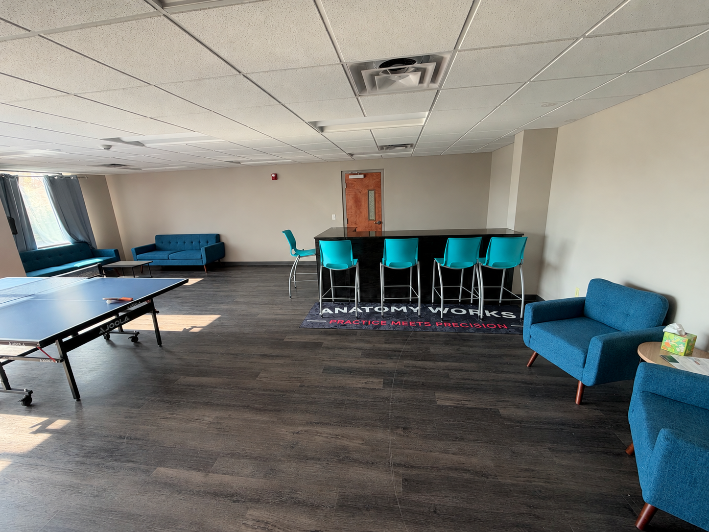 The Anatomy Works lounge — couches, high-top tables, and the Anatomy Works floor mat